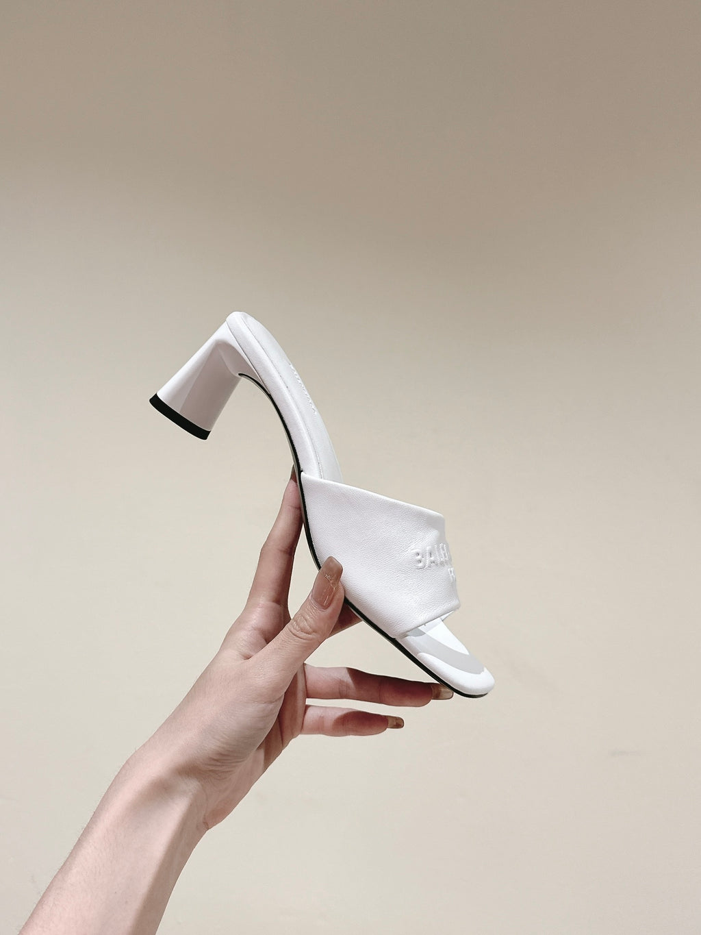 White slide sandal with tall block heel and embossed Balenciaga logo, held up