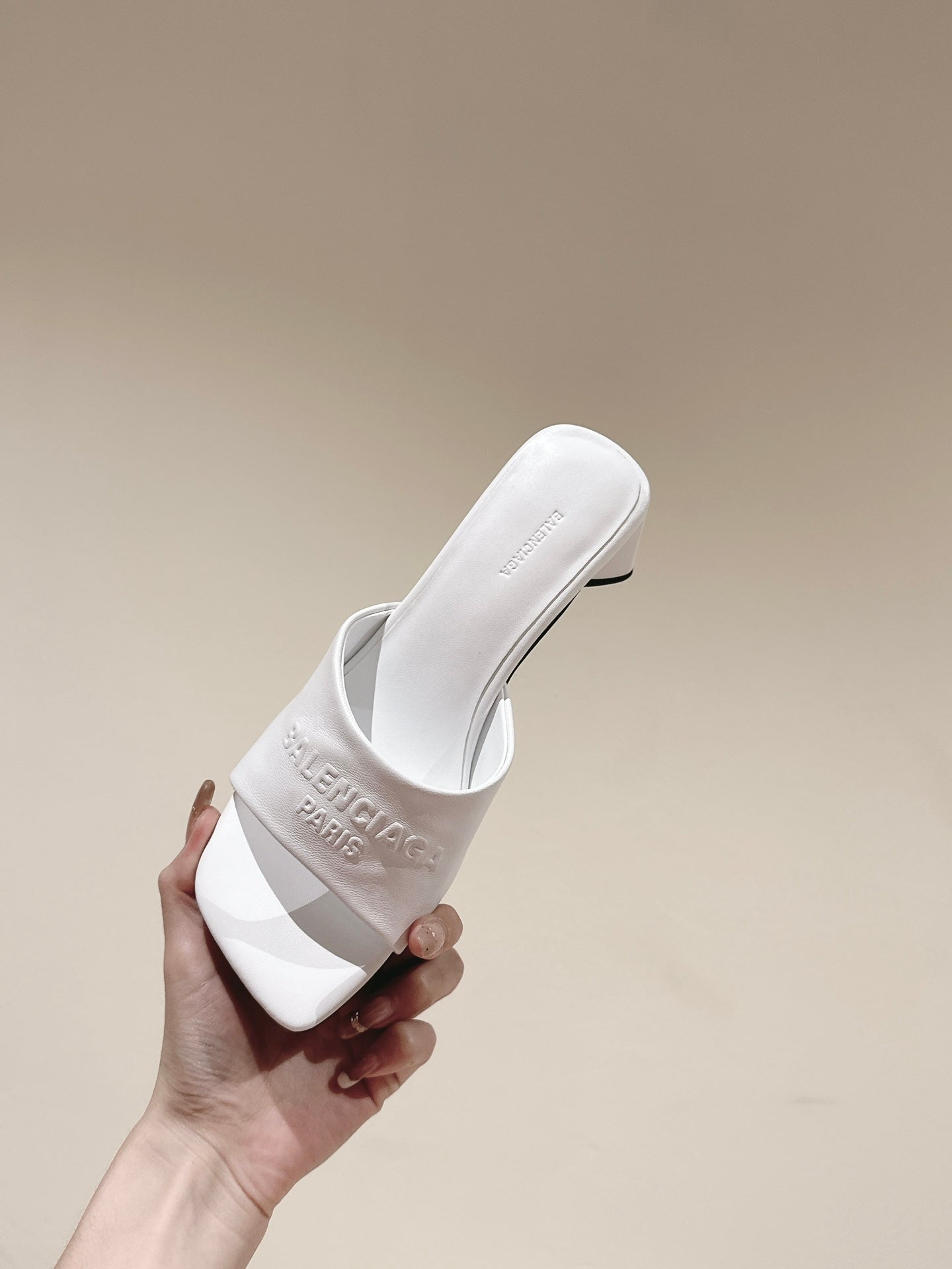White slide sandal with embossed Balenciaga logo on strap, held in hand