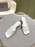 White slide sandals with embossed Balenciaga branding and wide strap, angled pair
