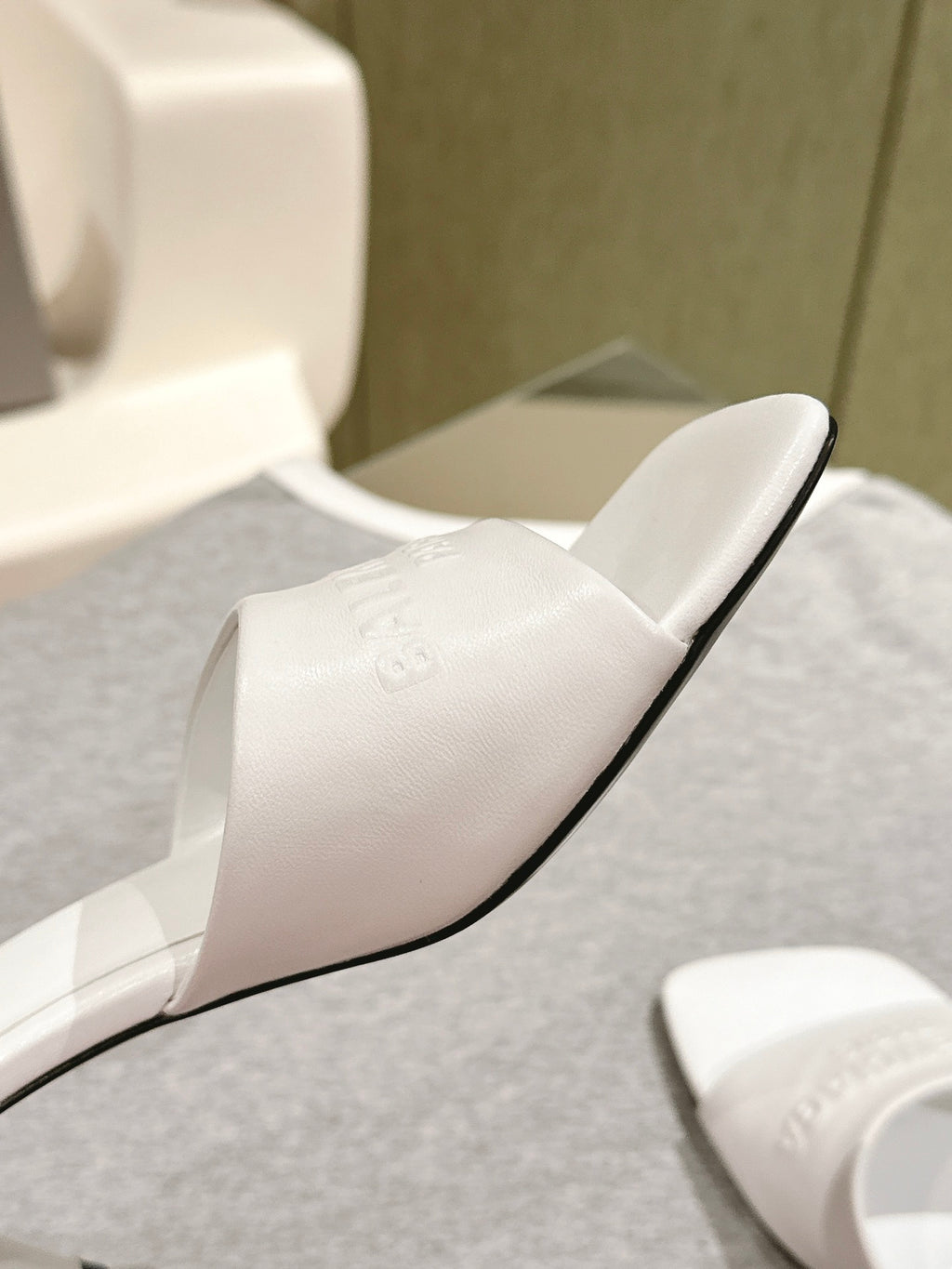 White slide sandal close-up with black sole edge and embossed logo on strap