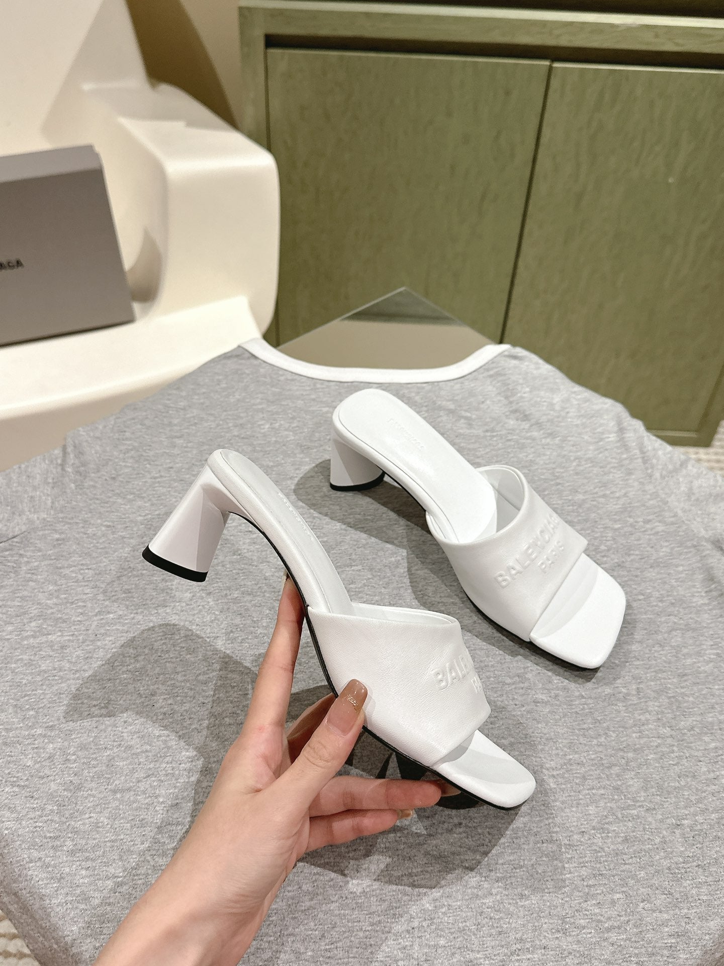 White slide sandal with black-edged block heel and embossed Balenciaga logo, held