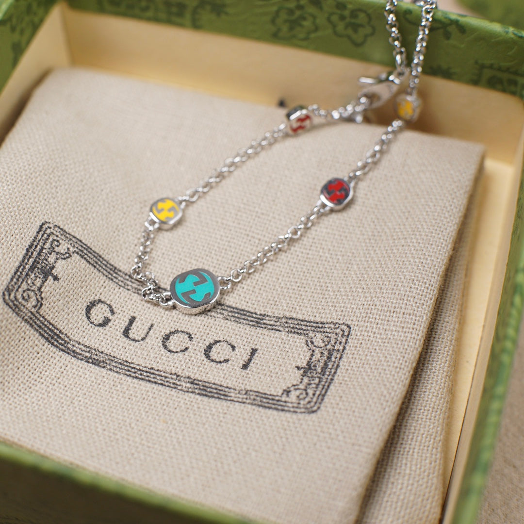 Gucci charm bracelet displayed on fabric pouch, silver chain with enamel charms