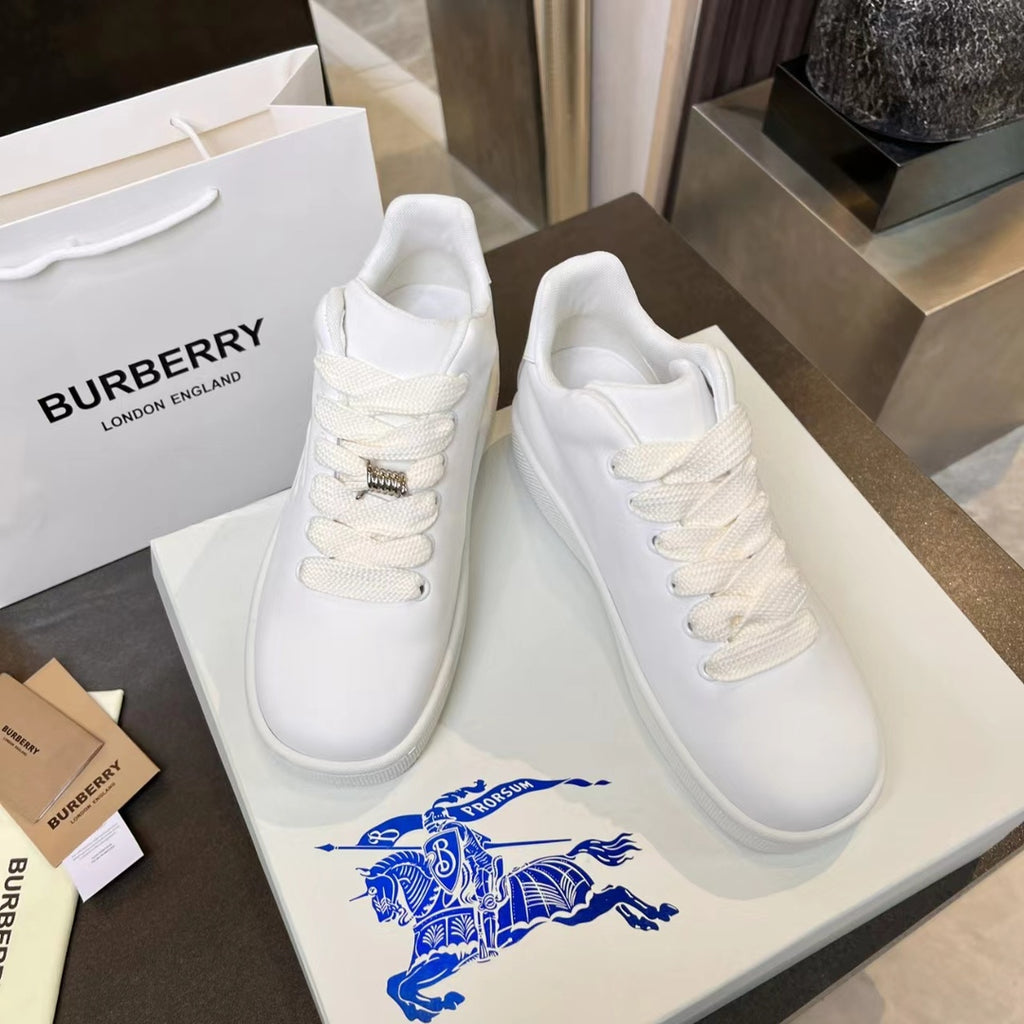 Pair of white lace-up sneakers on box, with textured logo hardware
