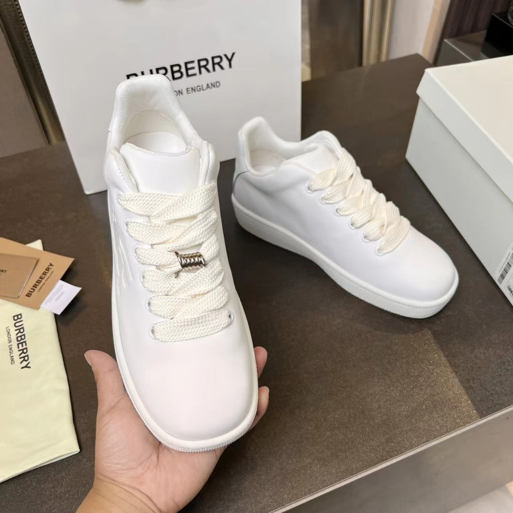 White leather lace-up sneakers held in hand, with gold-tone logo on lace tab