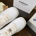 Close-up of white lace-up sneaker with metal logo eyelet and rounded toe