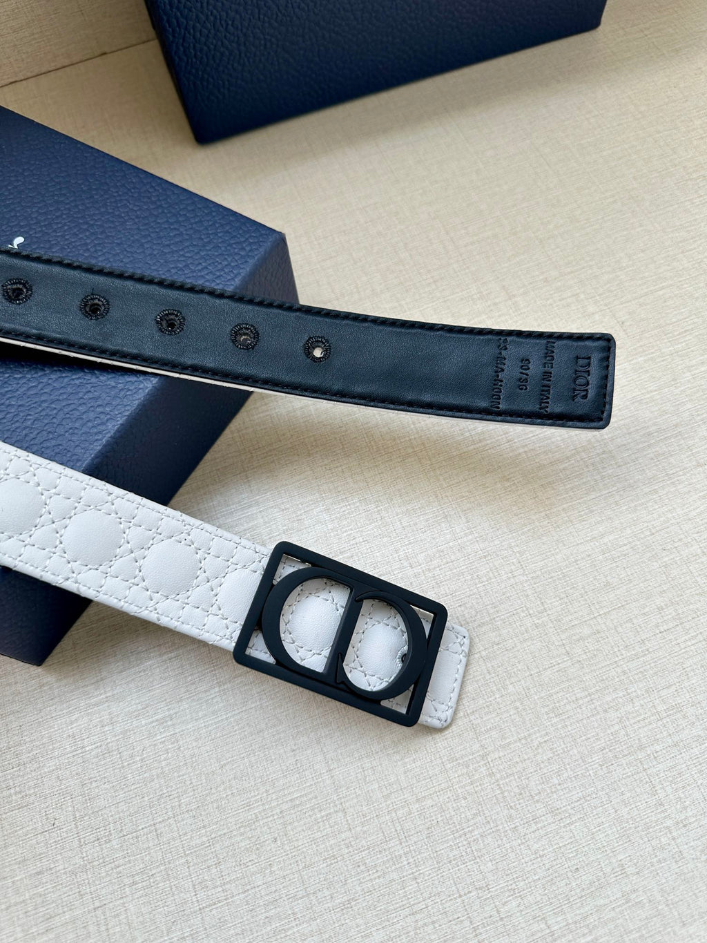 White belt strap detail with black buckle and rows of metal adjustment holes.