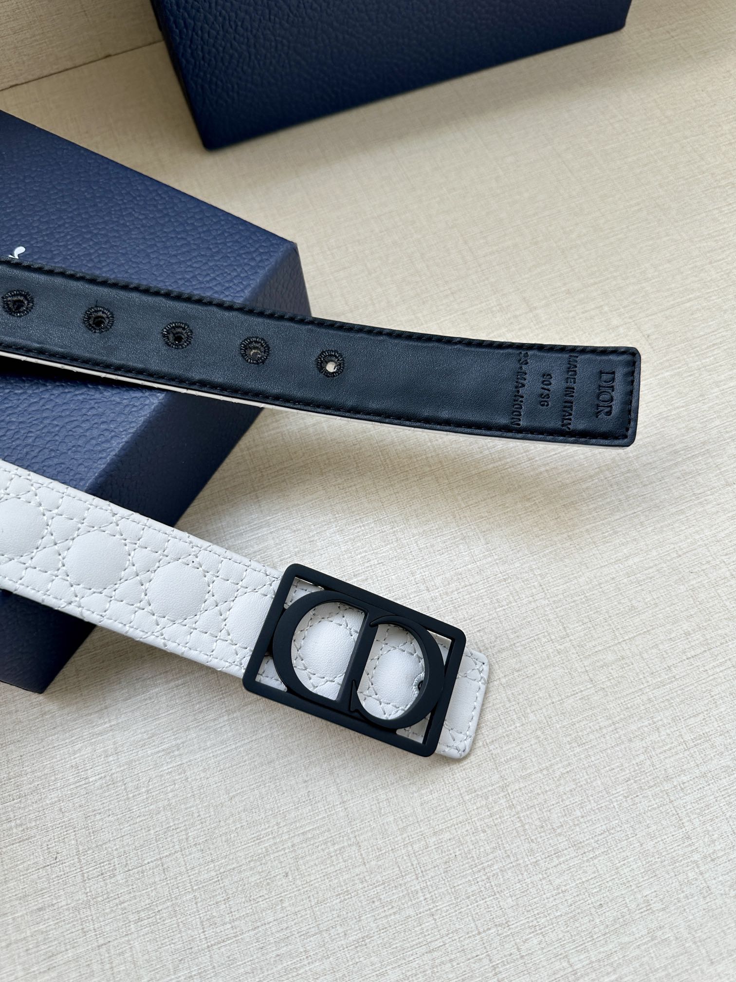 White belt strap detail with black buckle and rows of metal adjustment holes.