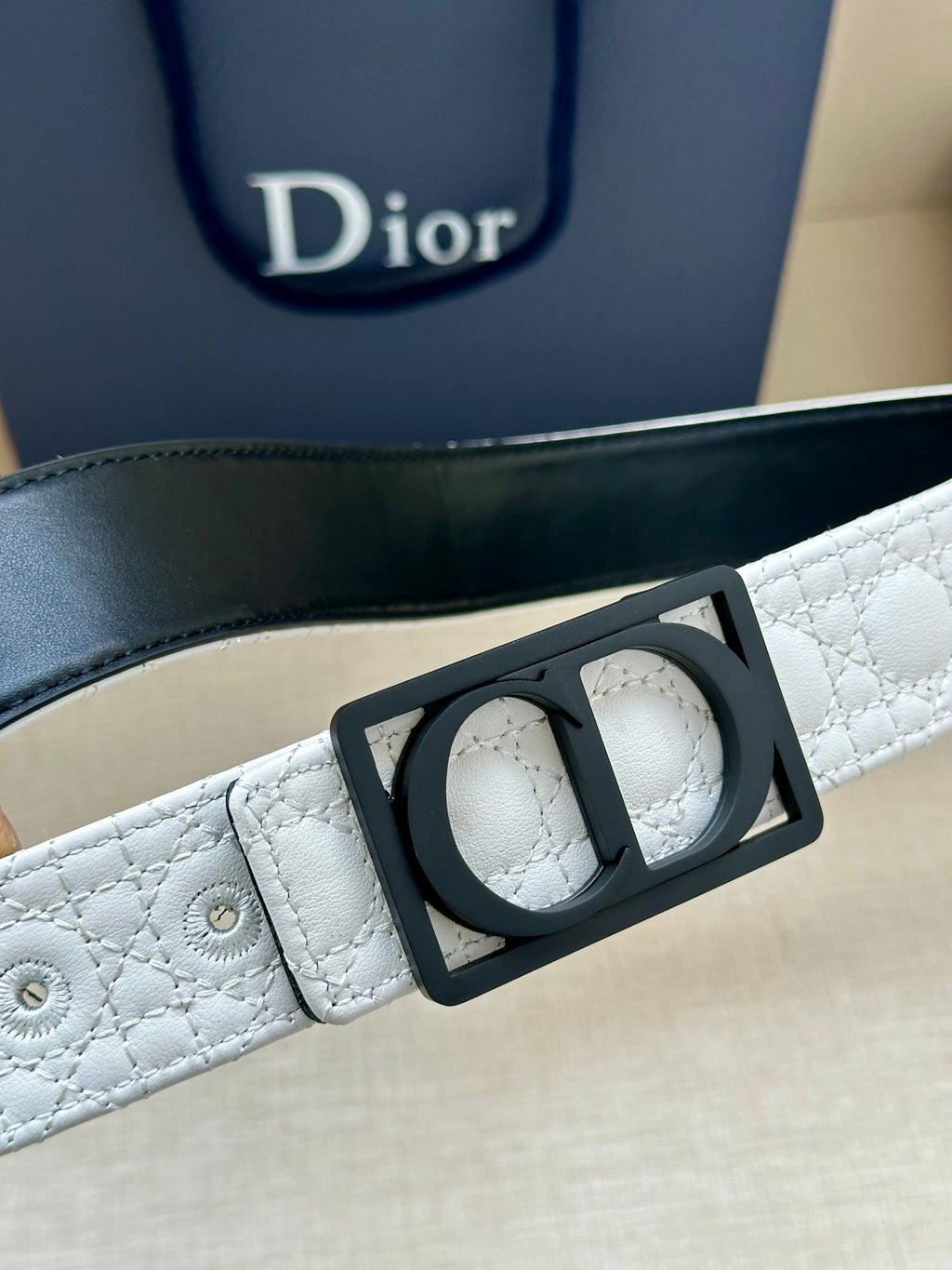 White belt close-up with black rectangular buckle and perforated strap holes.