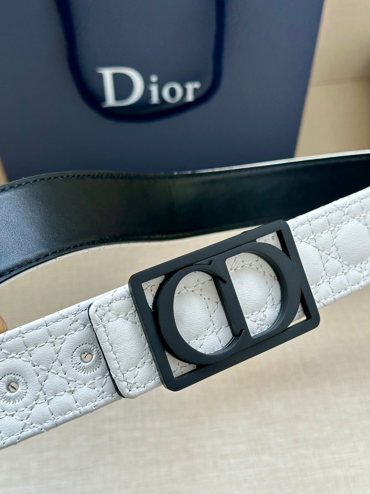 White belt close-up with black rectangular buckle and perforated strap holes.