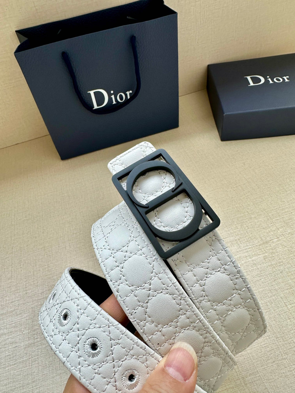 White leather belt with black Dior buckle shown from side angle, quilted texture.
