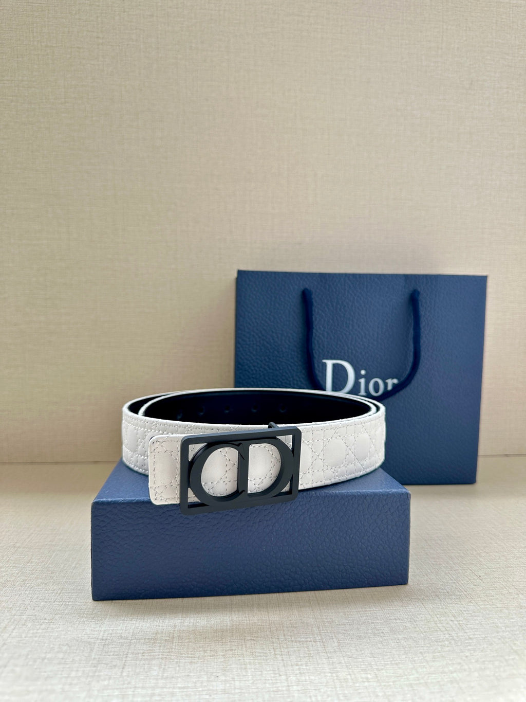 White Dior belt with black square buckle centered on navy gift box.