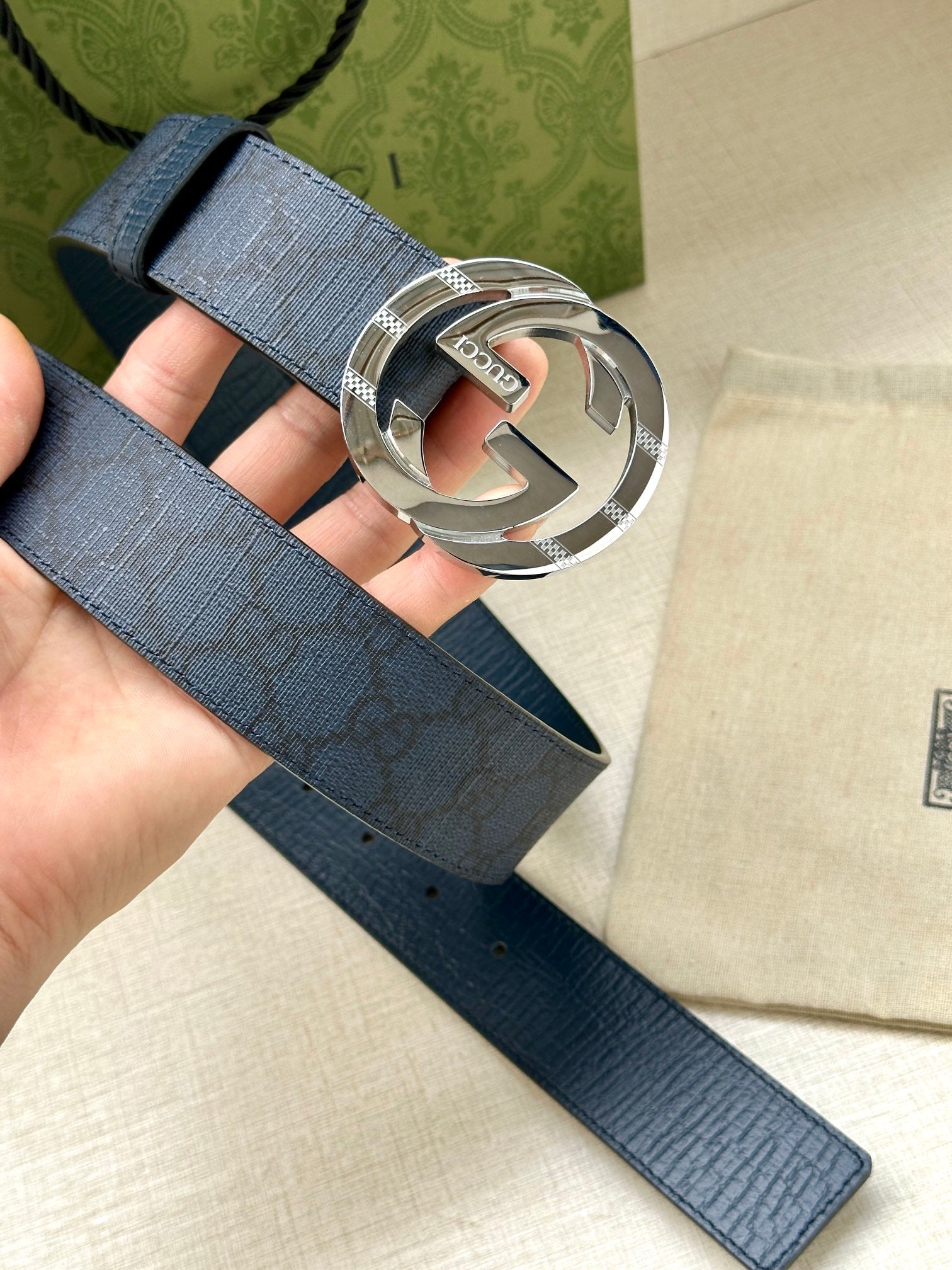 Gucci belt buckle close-up on dark blue strap, silver interlocking G logo