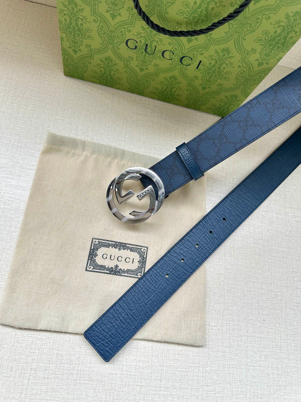 Gucci belt flat lay with dark blue strap and silver interlocking G buckle close-up