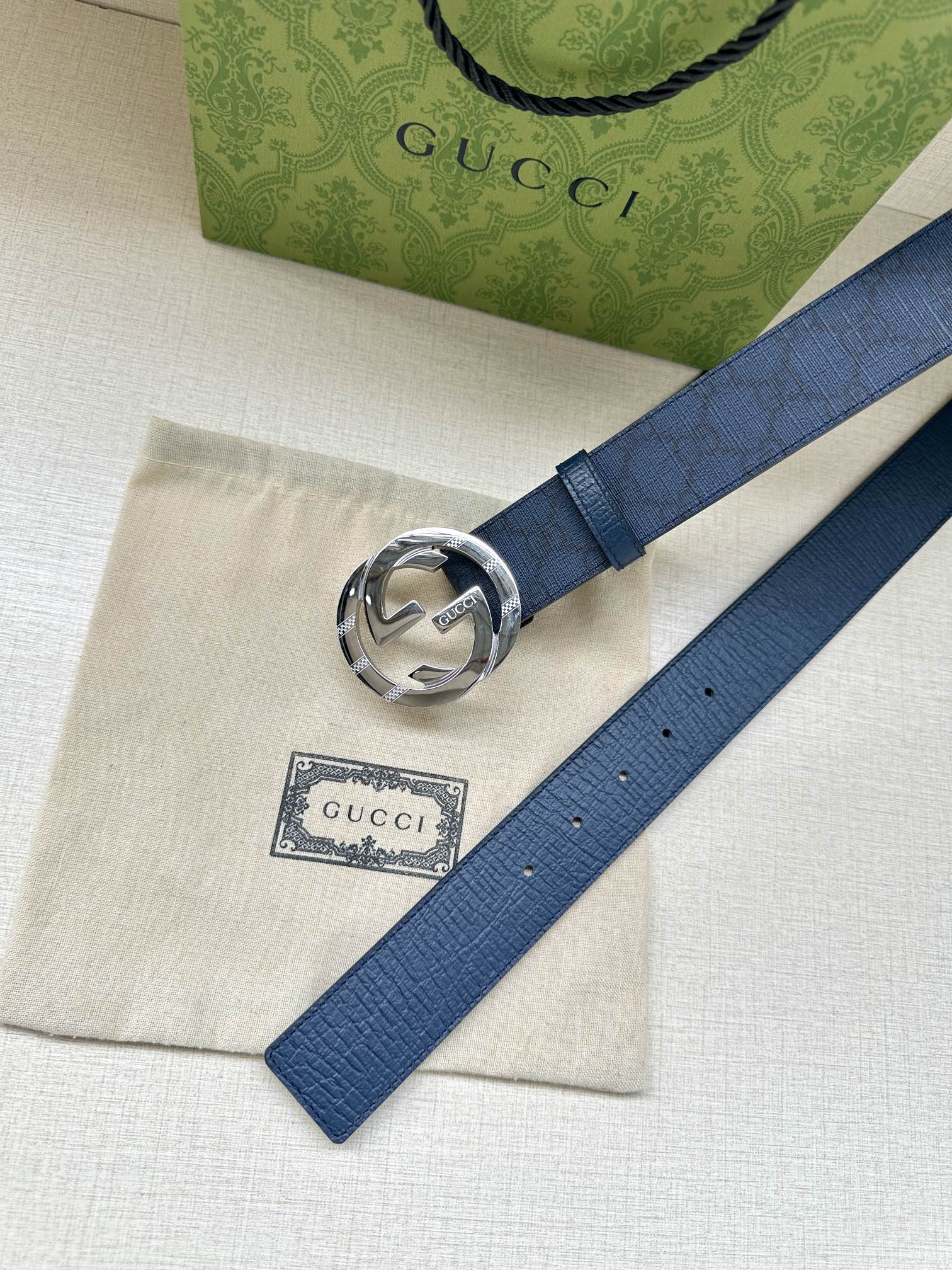 Gucci belt flat lay with dark blue strap and silver interlocking G buckle close-up