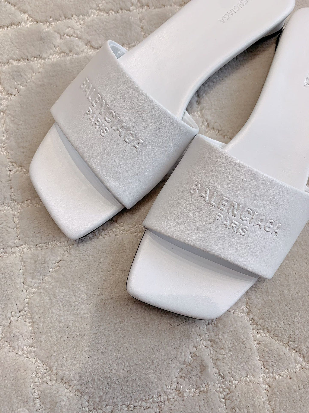 White Balenciaga slide sandals close-up with embossed text on front strap and footbed
