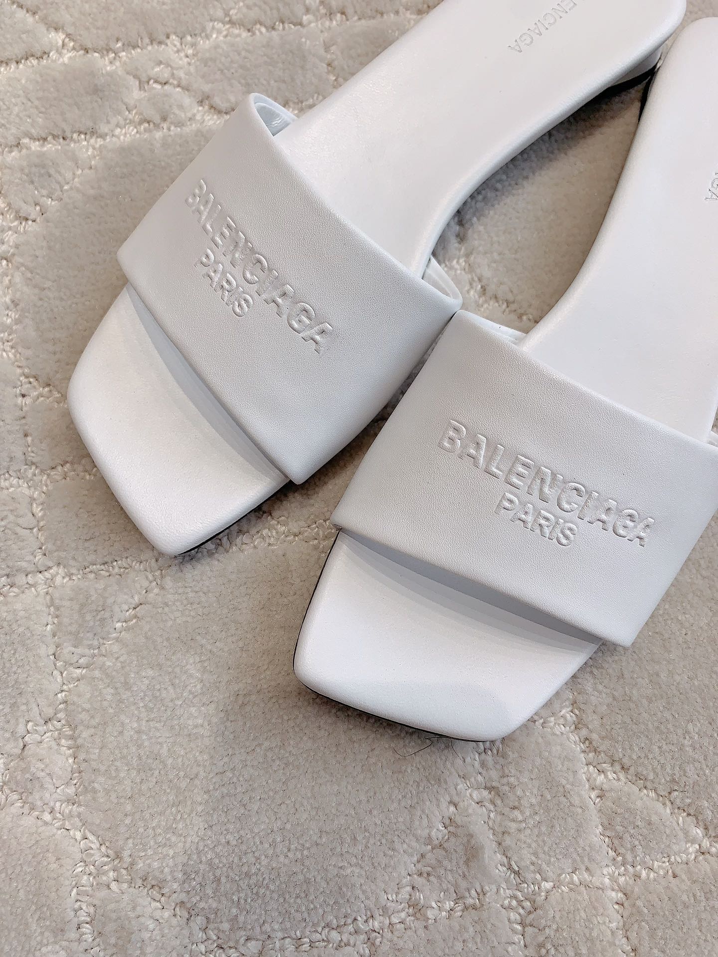 White Balenciaga slide sandals close-up with embossed text on front strap and footbed