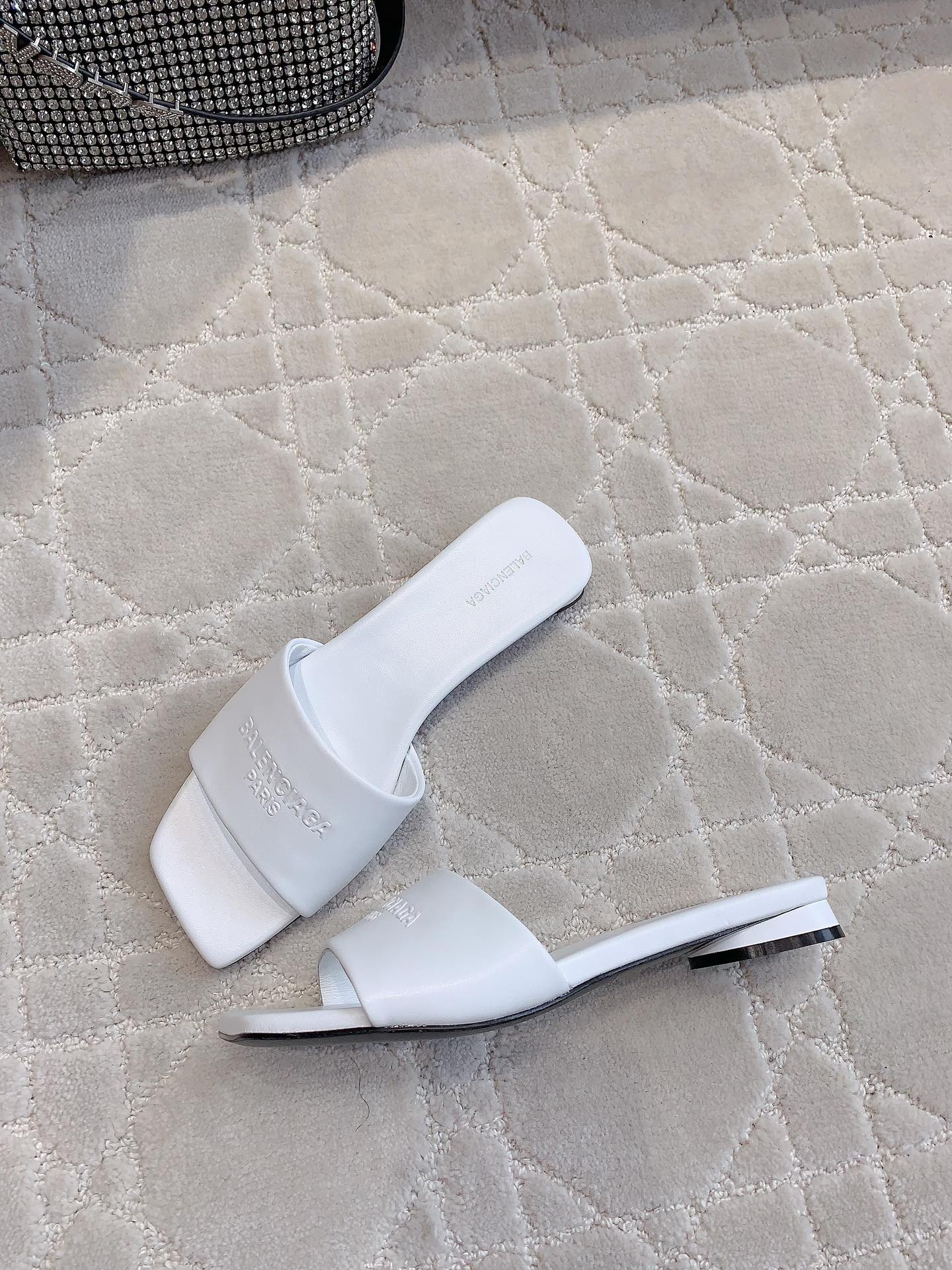 White Balenciaga slide sandals with metal-look heel detail and embossed logo strap