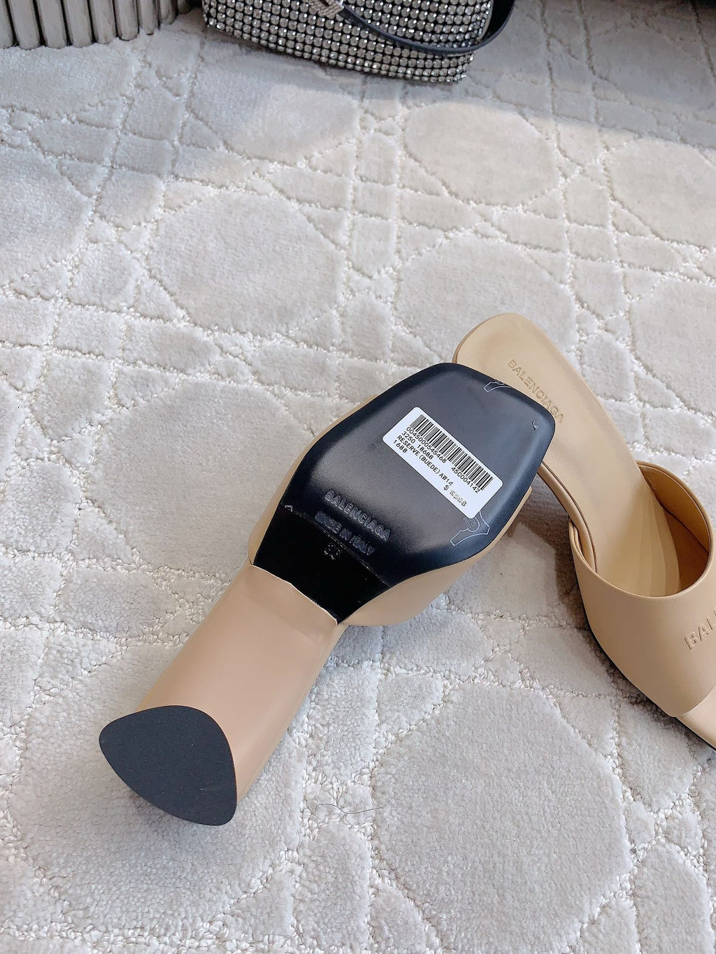 Beige slide sandal with black underside label and barcode tag, angled