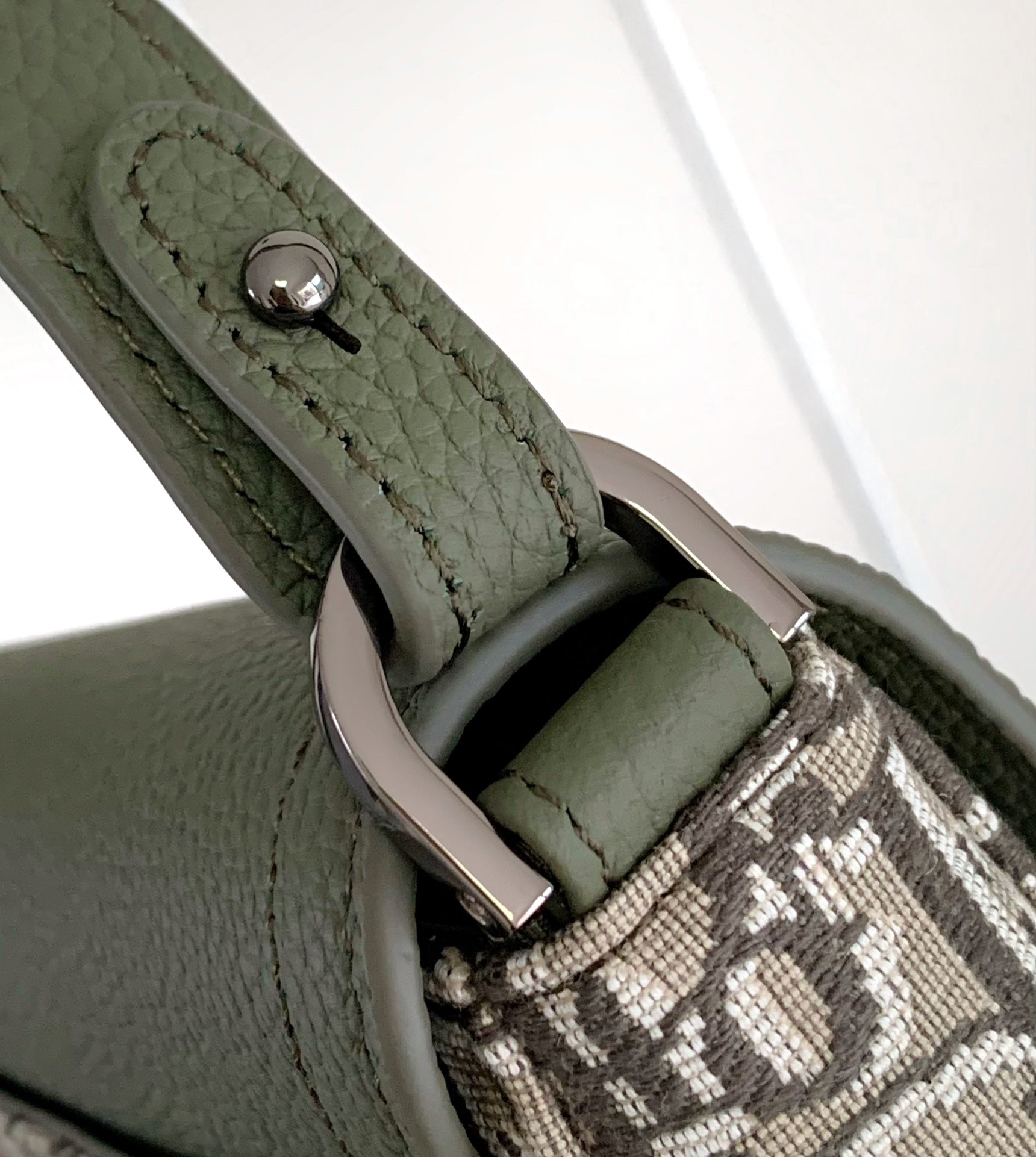 Green strap with buckle and stitched edge on a beige monogram crossbody bag