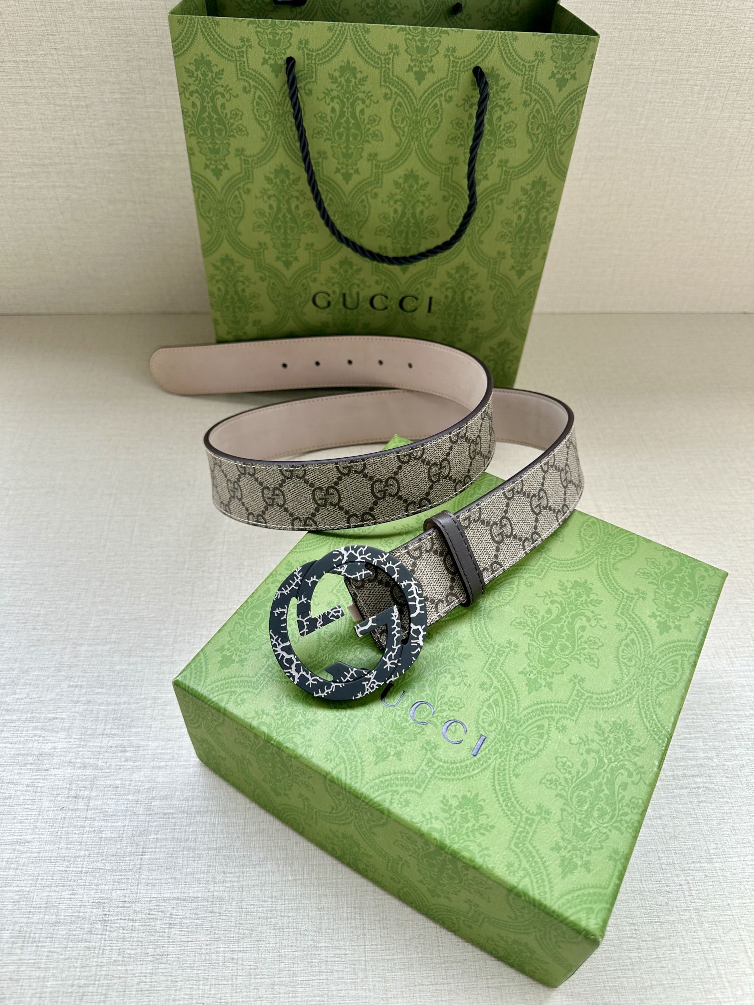 Gucci belt with beige GG canvas, black-and-green patterned buckle, pink underside