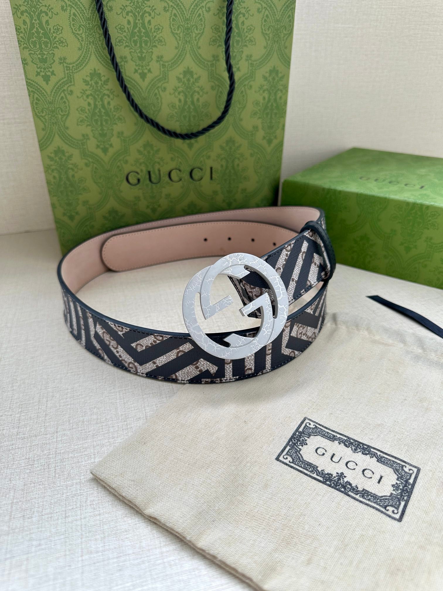 Gucci monogram belt with light grey circular buckle, navy-and-white pattern strap and pink underside