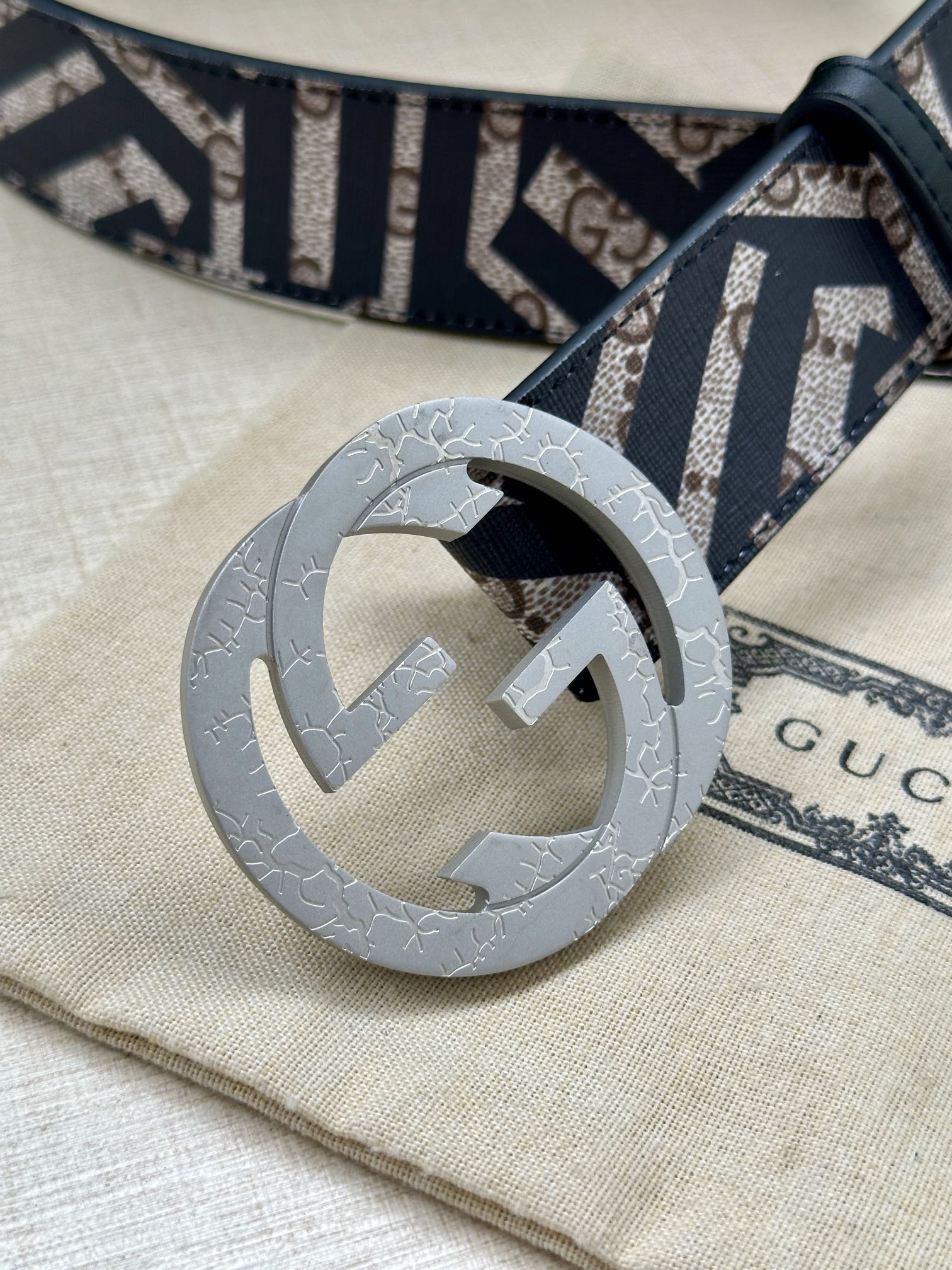Gucci belt close-up with navy-and-white monogram strap and light grey interlocking buckle