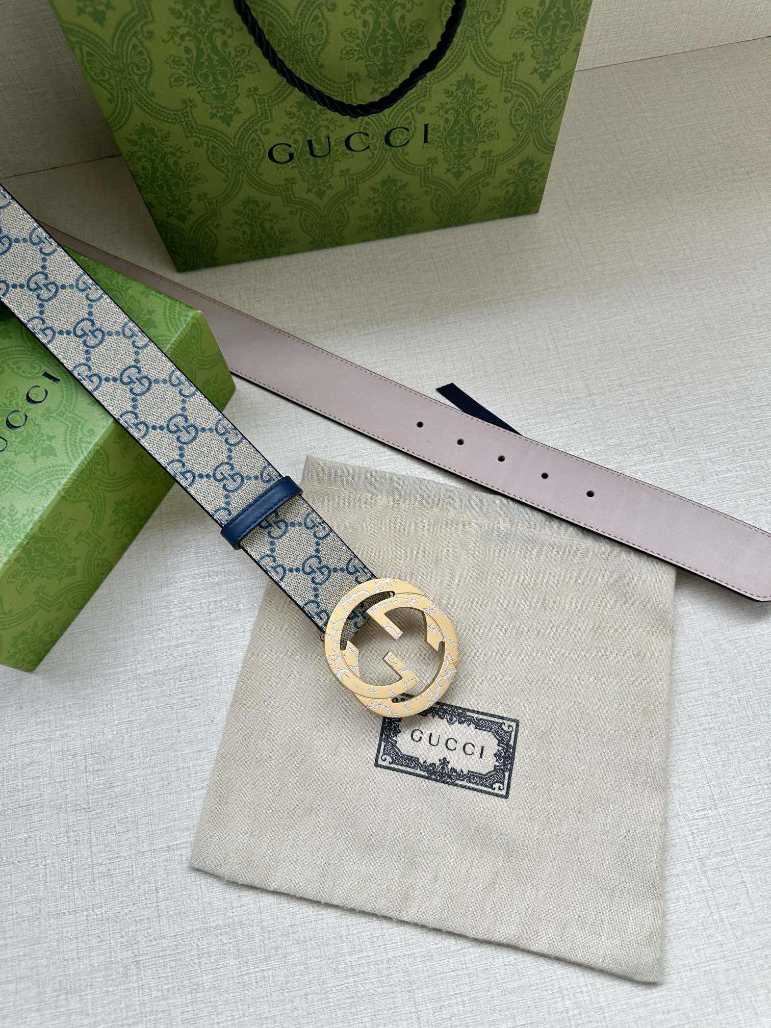 Gucci belt close-up of light pink underside and GG canvas strap with gold circular buckle.