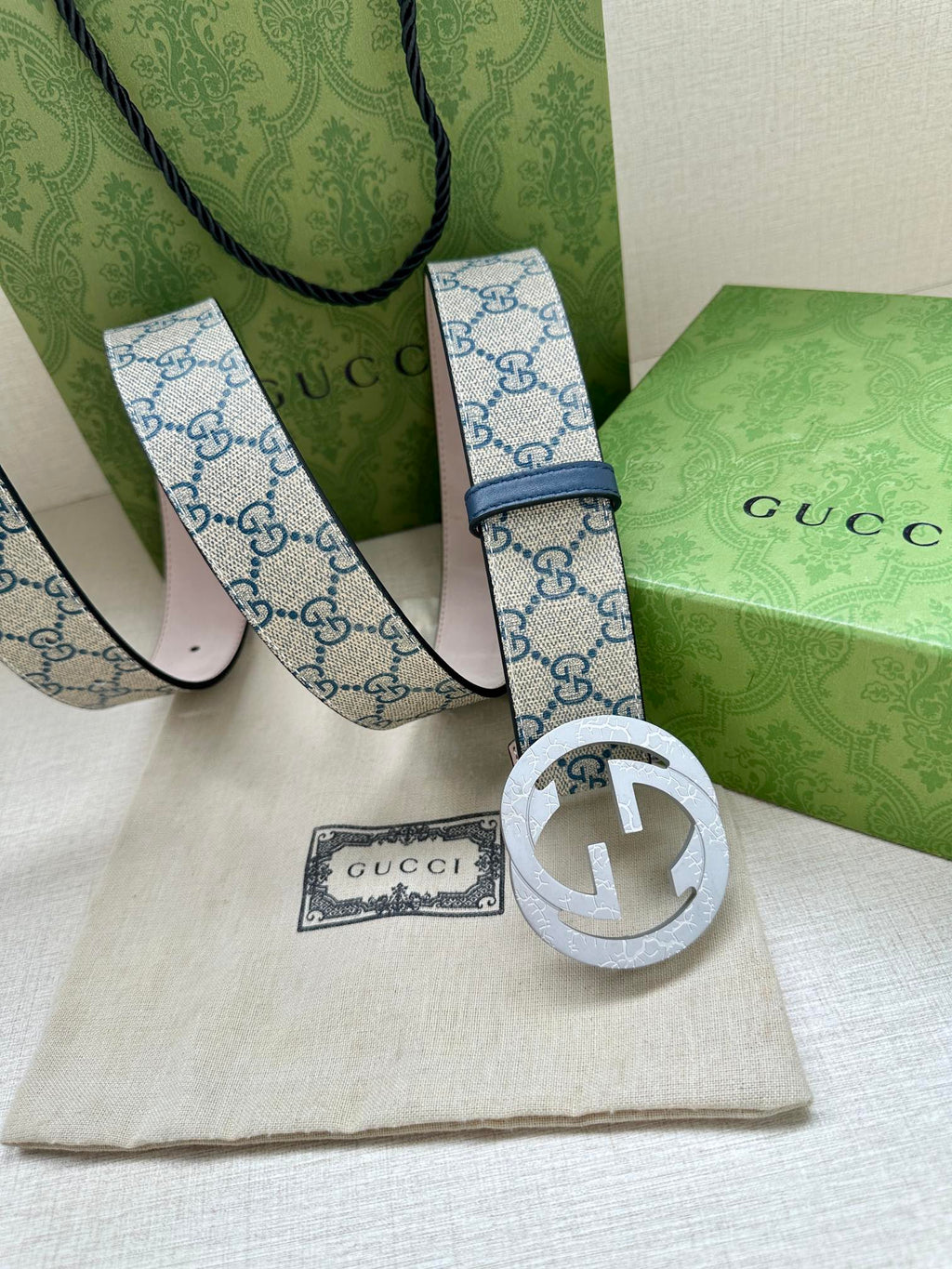 Gucci belt showing buckle and GG canvas strap with blue trim and adjustable holes.