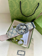 Gucci belt with GG canvas strap and round logo buckle, laid across green gift box.