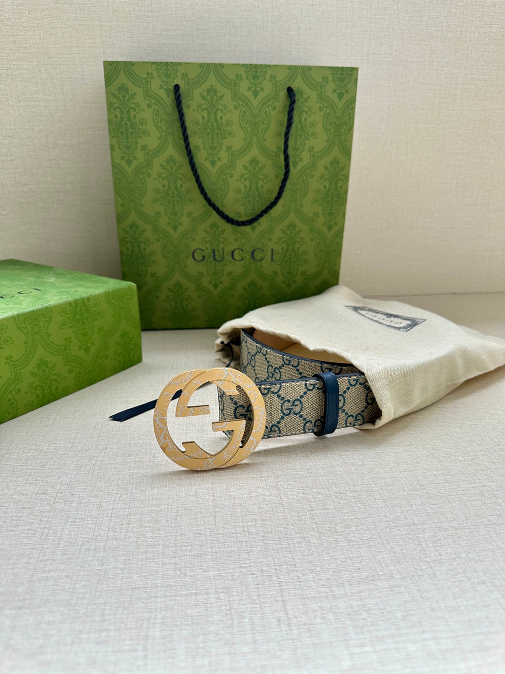 Gucci belt with GG canvas strap and gold circular buckle resting on cream pouch.