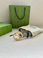 Gucci belt with GG canvas strap and gold circular buckle resting on cream pouch.