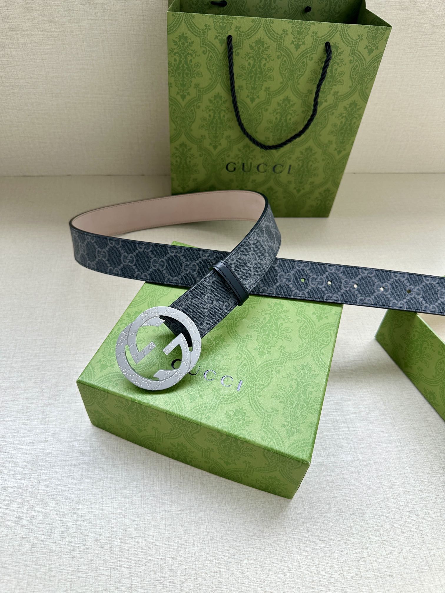 Gucci belt laid out with round silver-toned GG buckle on green box