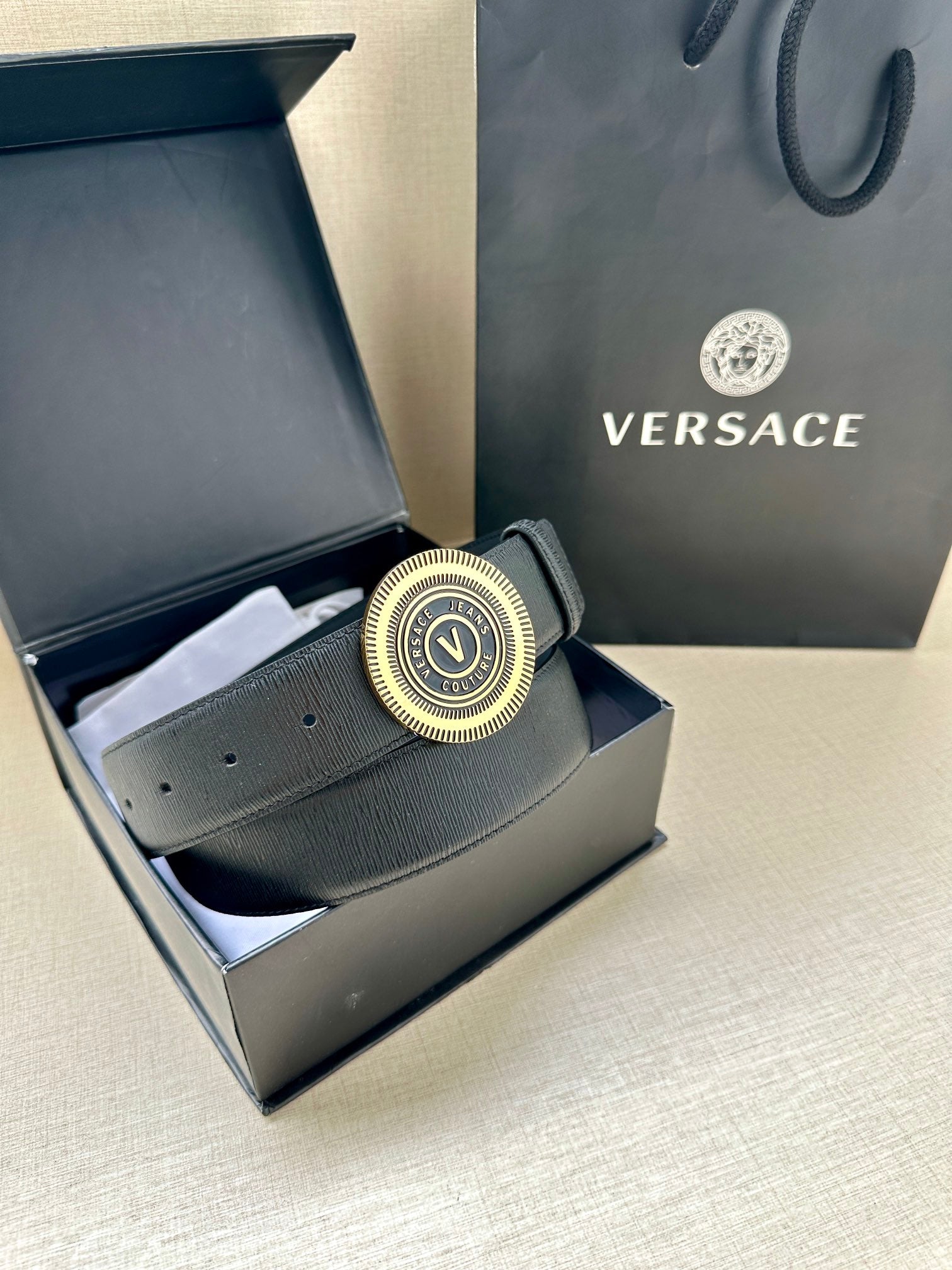 Dark blue leather belt with gold circular logo buckle in box