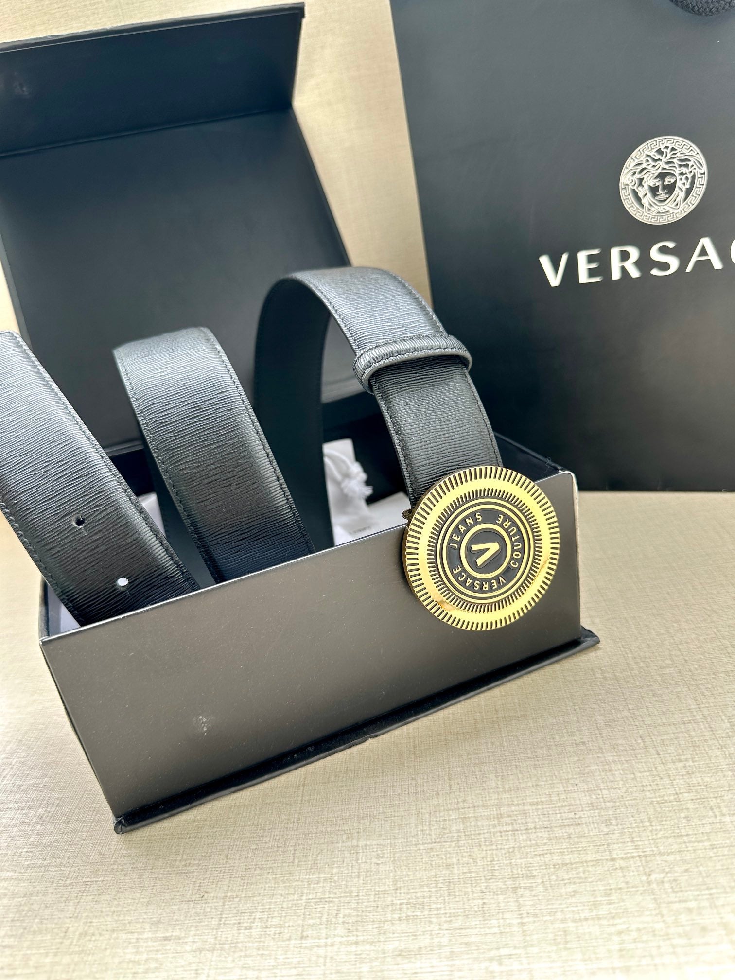 Dark blue leather belt with circular gold logo buckle