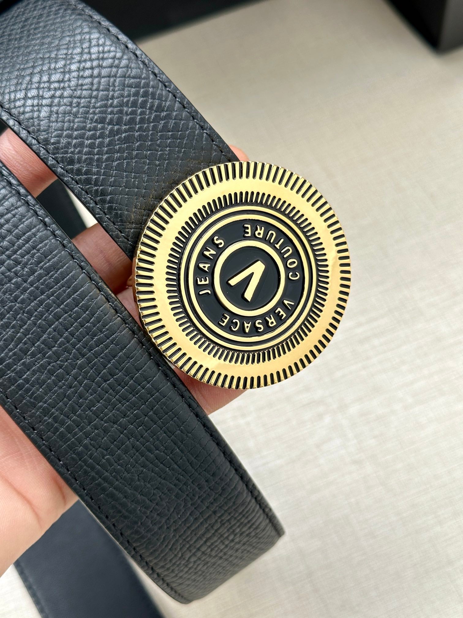 Versace belt buckle close-up with circular gold-tone crest on dark blue leather