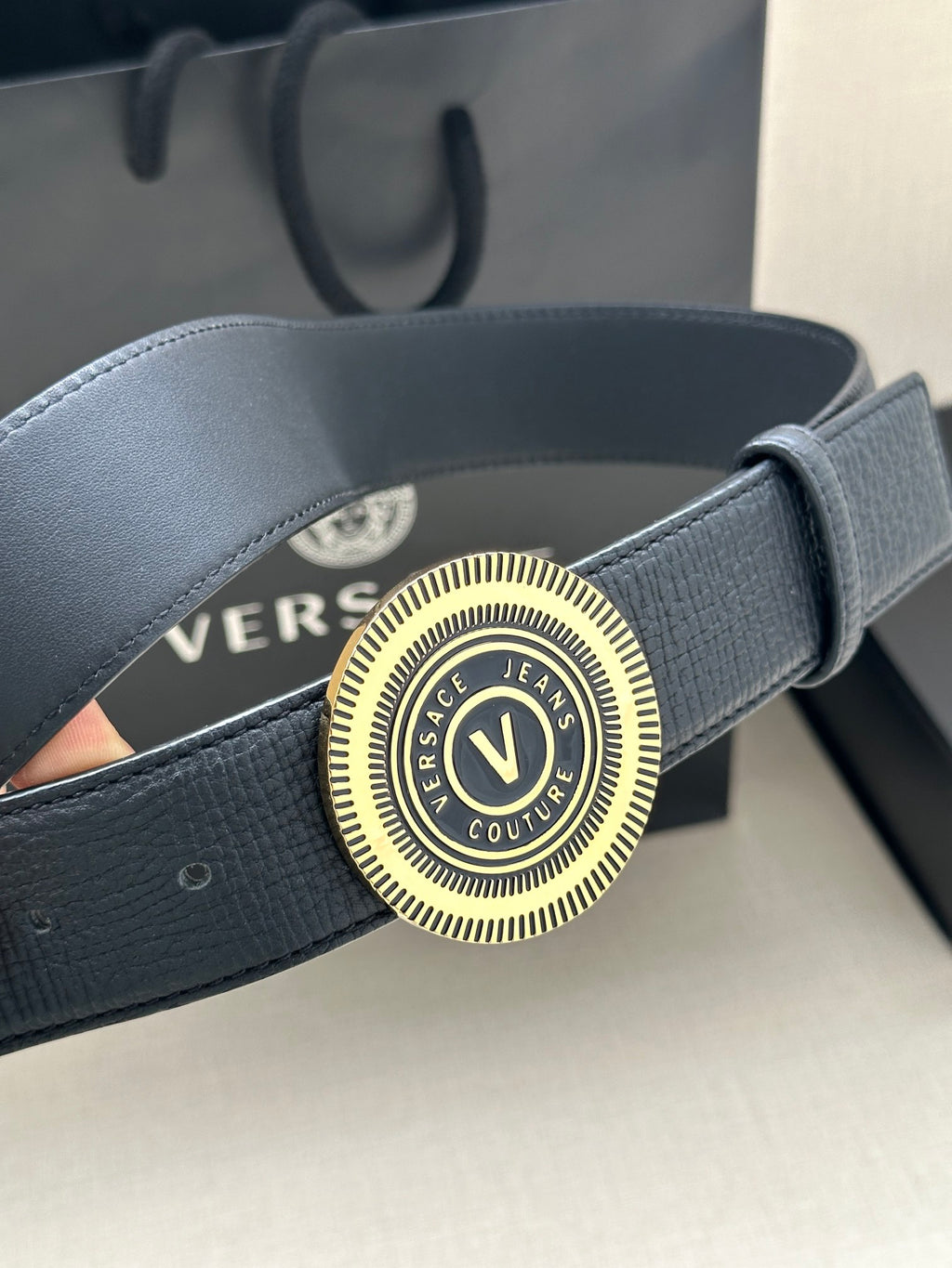 Versace belt close-up: dark blue leather with circular gold-tone logo buckle