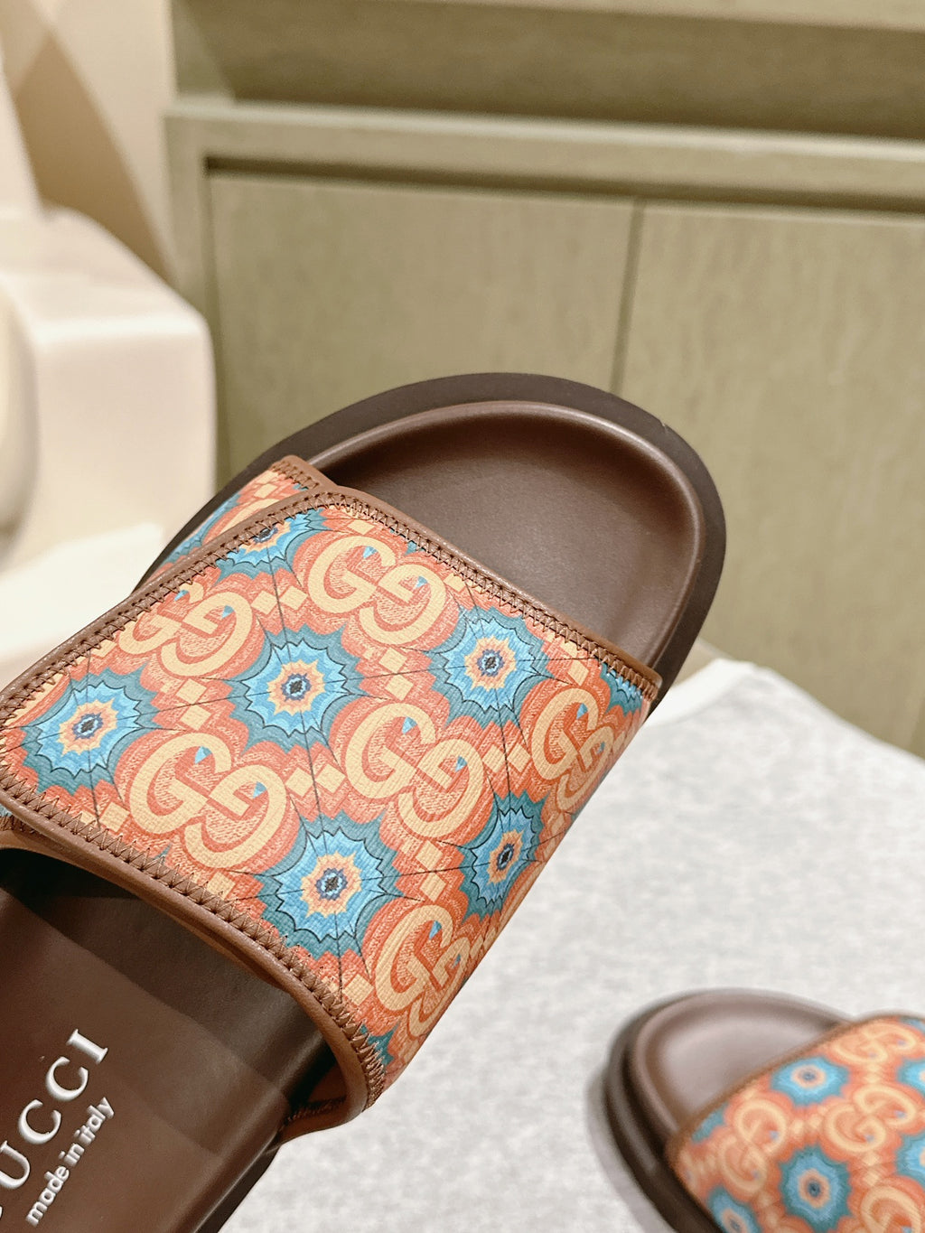 Close-up of brown slide sandals showing multicolor patterned strap and interior branding