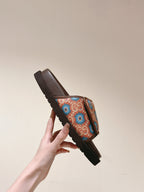Hand holding a brown slide sandal with multicolor patterned strap and ribbed outsole