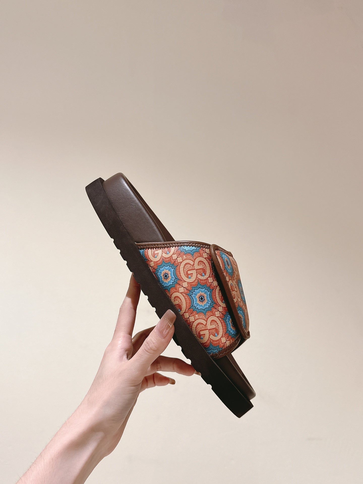 Hand holding a brown slide sandal with multicolor patterned strap and ribbed outsole