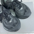 Pair of dark gray/black lace-up unisex sneakers on a box, showing side logos and panels