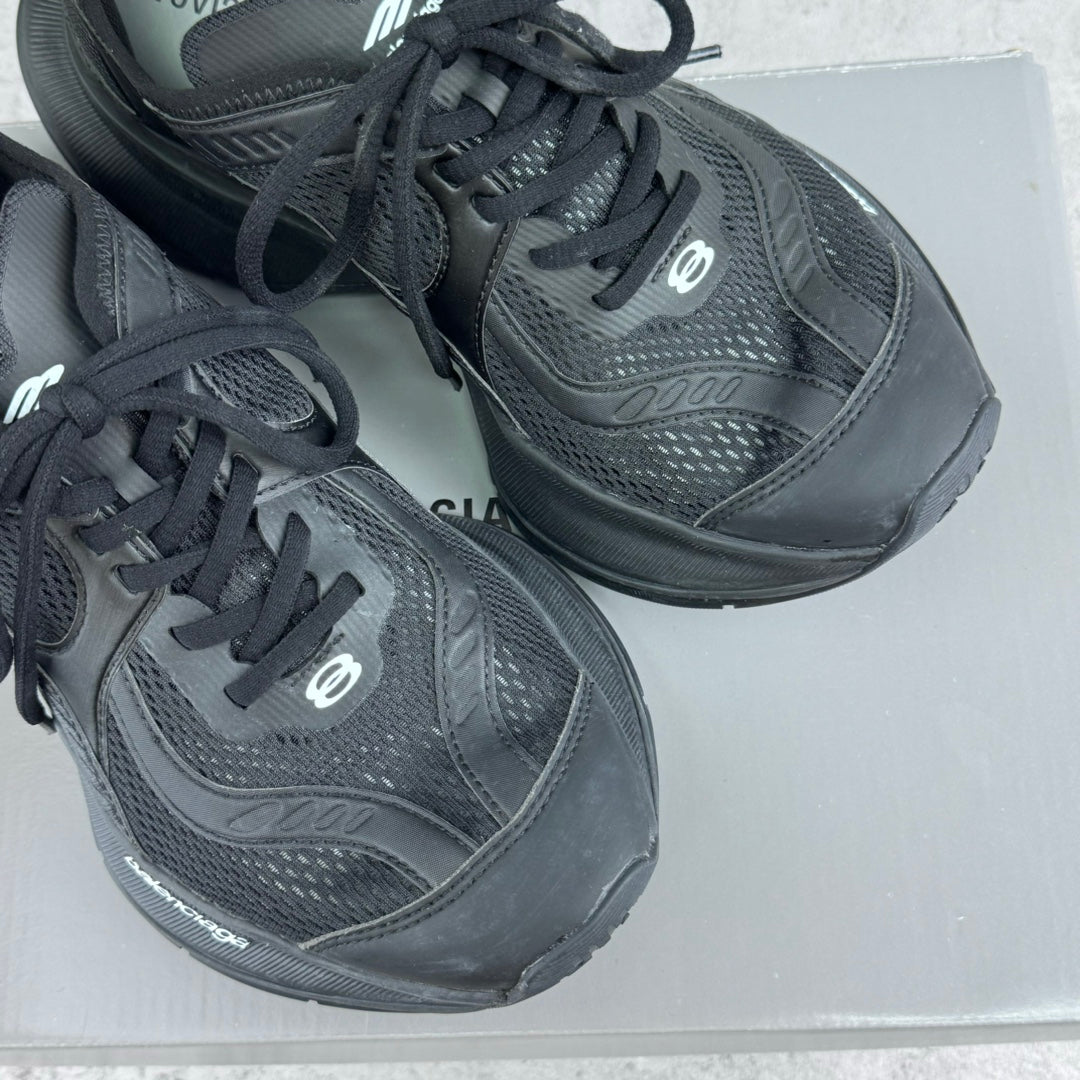 Pair of dark gray/black lace-up unisex sneakers on a box, showing side logos and panels