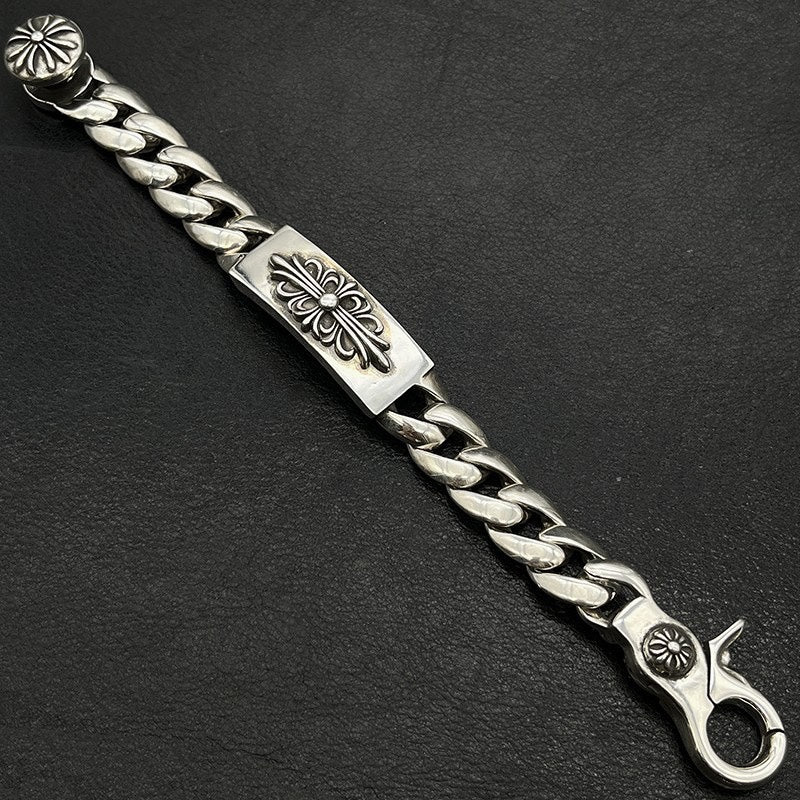 Silver-tone chain bracelet detail with engraved panel, flower medallion, and swivel clasp end