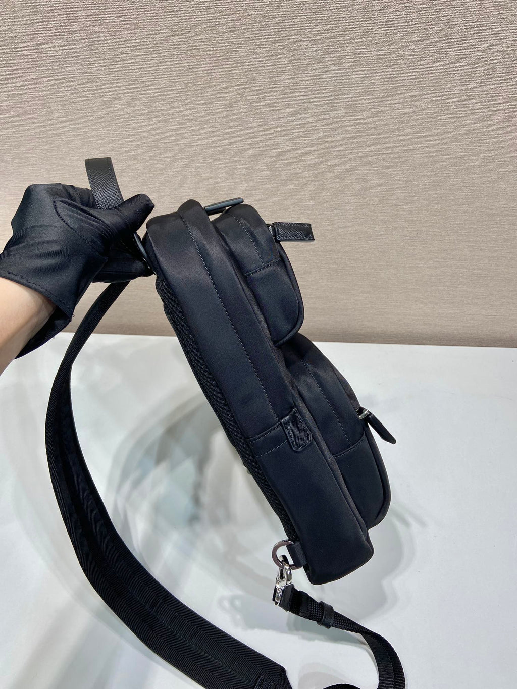 Black Prada mini backpack side view with strap and zipper pull, silver rings