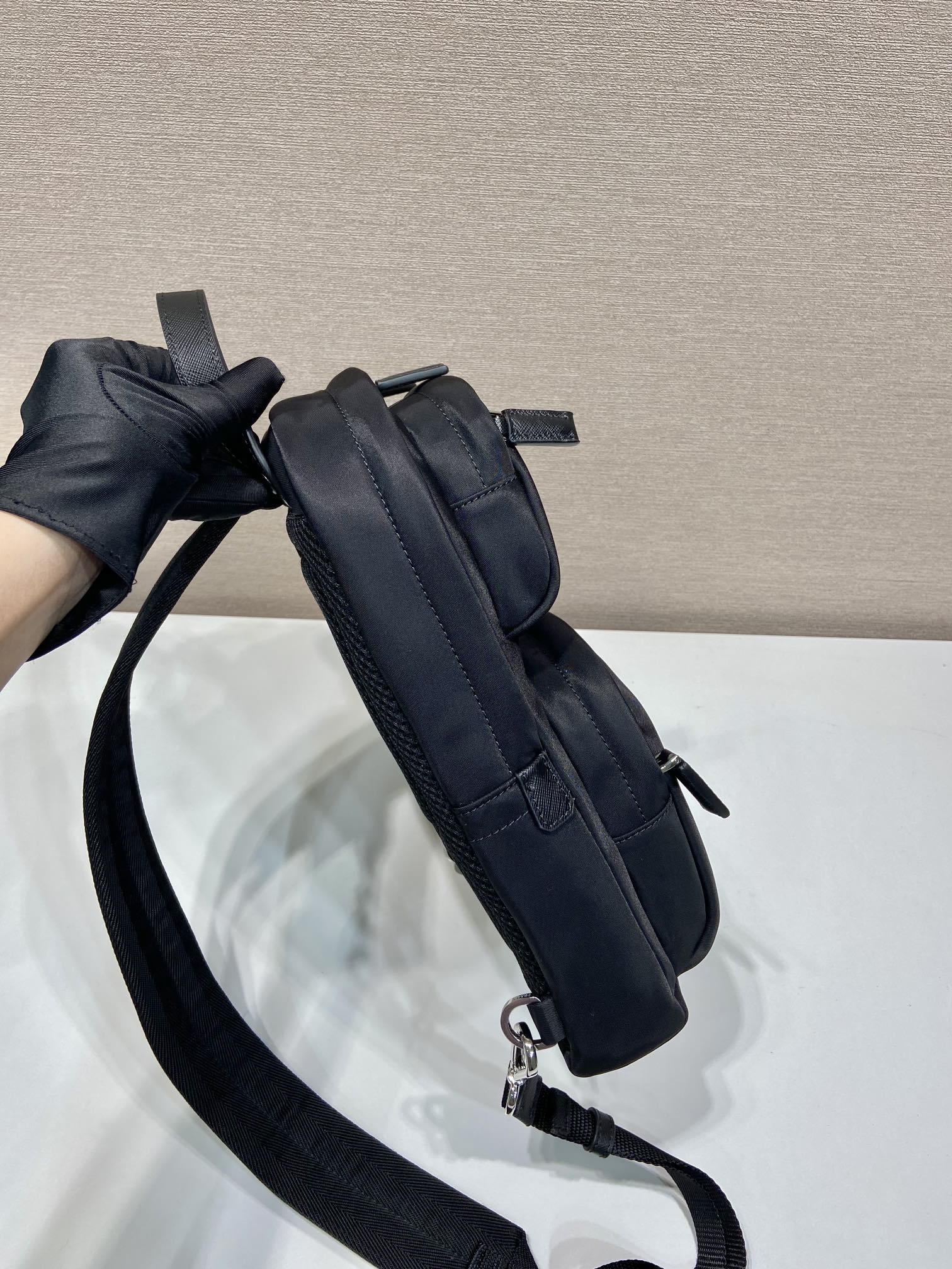 Black Prada mini backpack side view with strap and zipper pull, silver rings