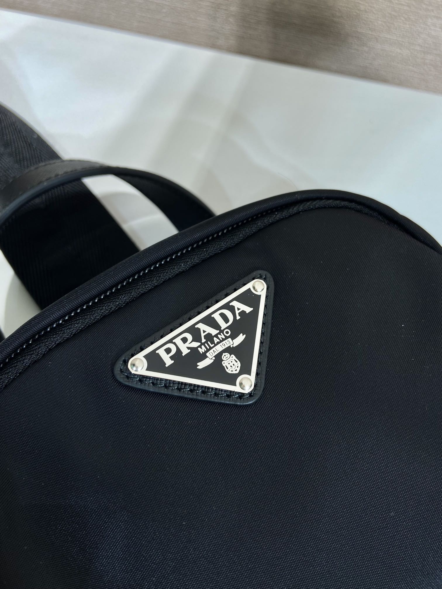 Prada logo patch on black mini backpack front, silver riveted label