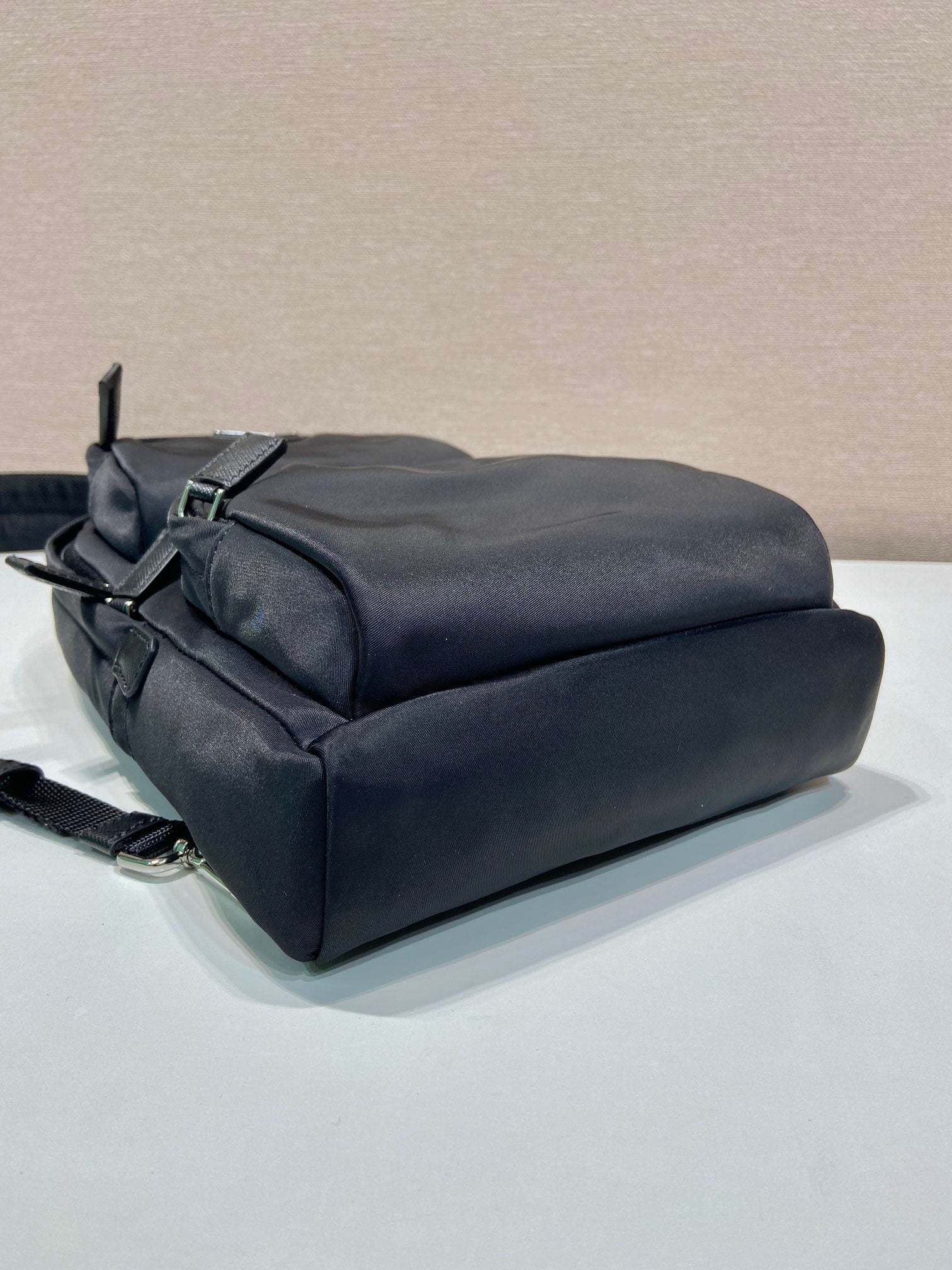 Black Prada mini backpack base with rolled top and side zip detail, metal hardware