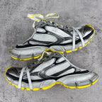 Gray and black chunky sneakers with white laces and yellow outsole trim, side view.