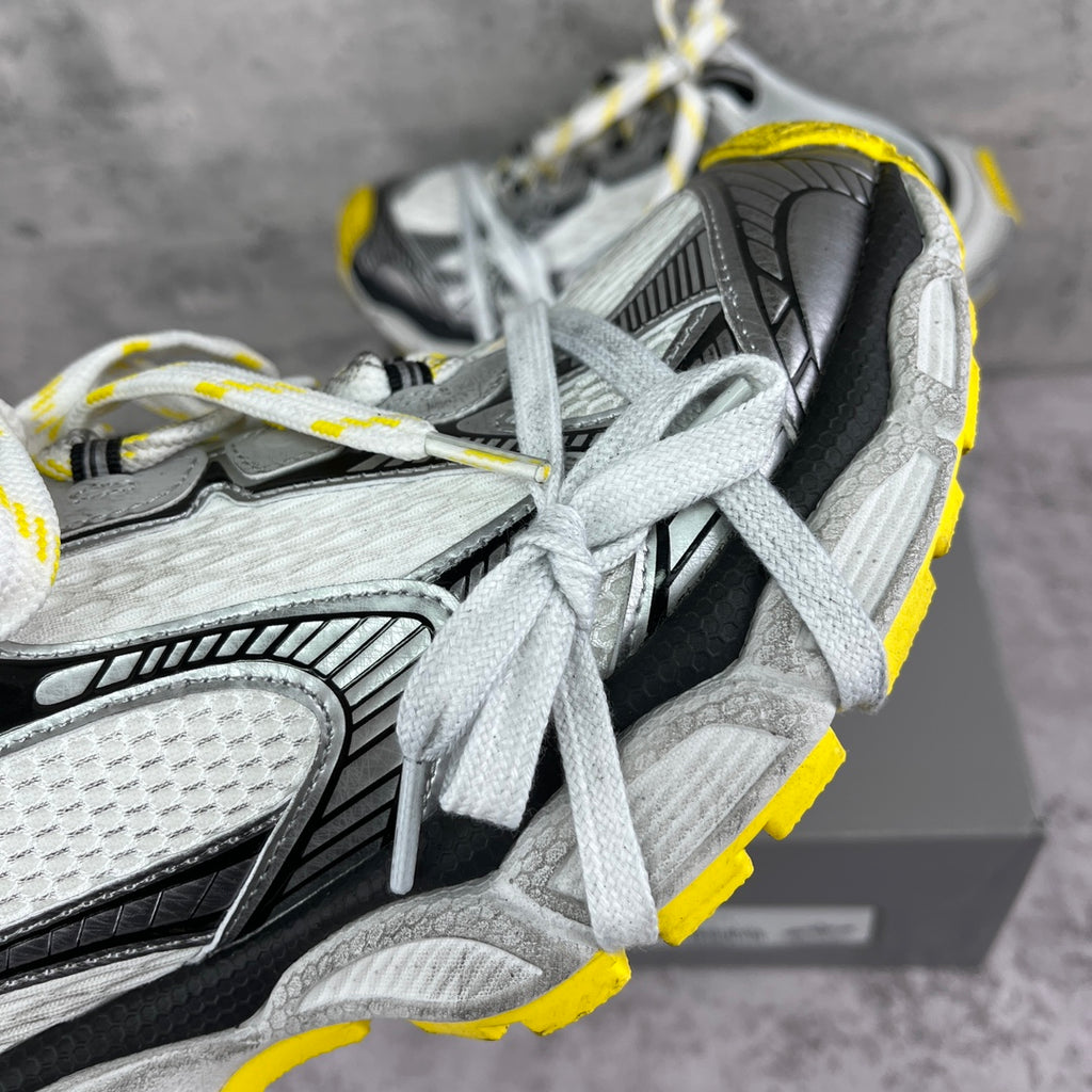 Close-up of gray and black chunky sneaker uppers with white laces and yellow edge.