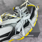 Close-up of gray and black chunky sneaker uppers with white laces and yellow edge.
