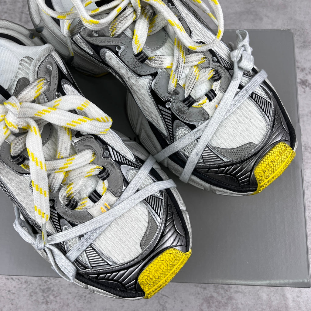 Gray and black chunky sneakers with white laces and yellow heel accents on box.